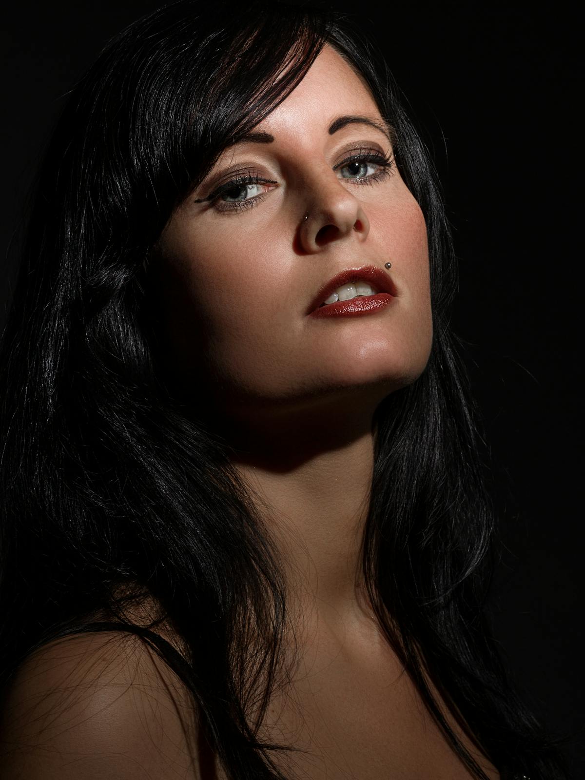 Carmen Vela photographed in dramatic studio light, dark hair pulled back, fixed expression.