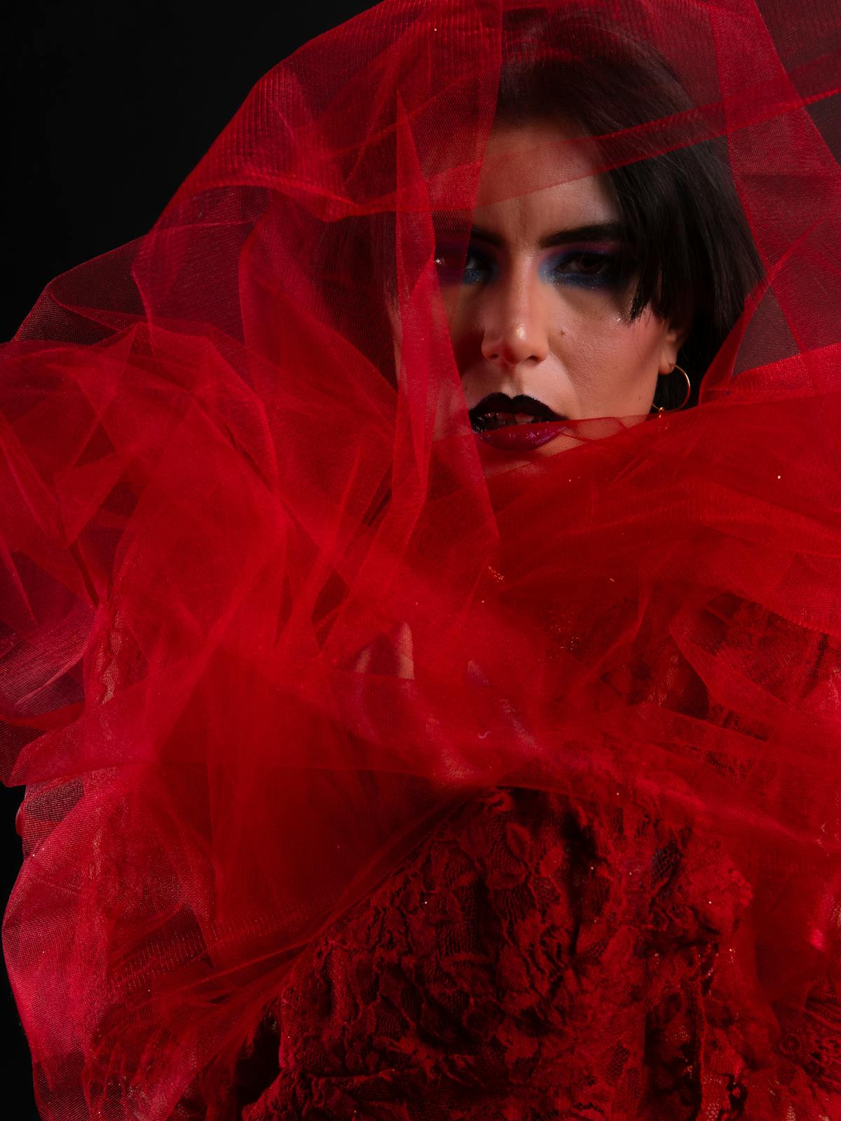 Backstage portrait — red lighting, draped fabric, smudged makeup.